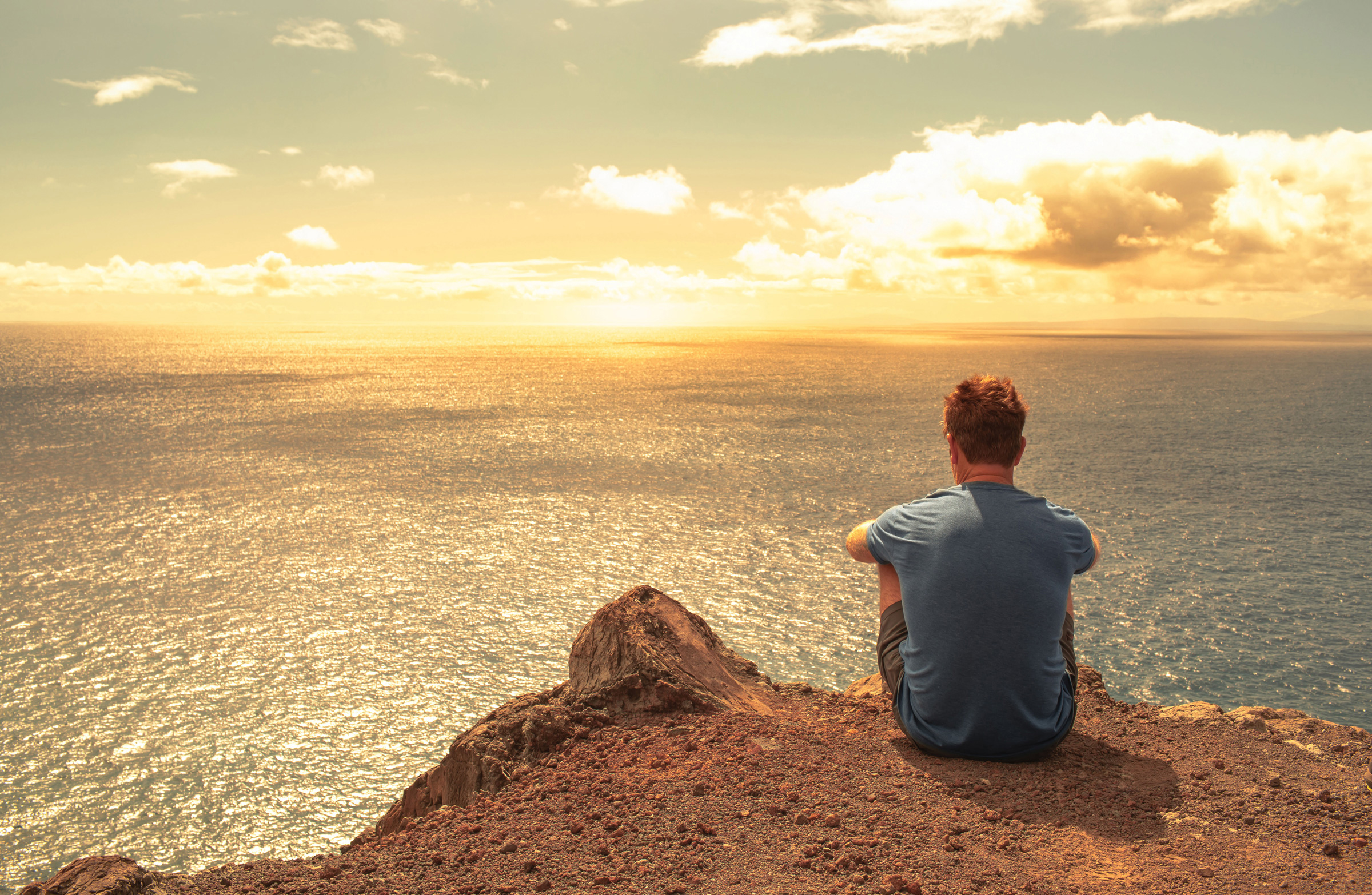 Man sits on cliff overlooking ocean view after scheduling a wealth management consultation with Fund Direct Advisors